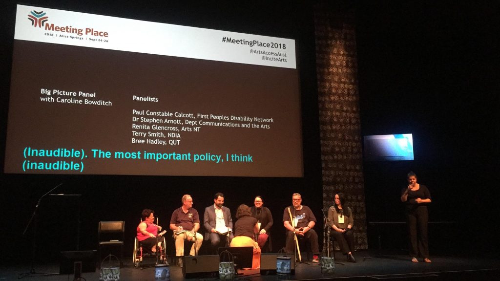 Menschen mit und ohne Behinderungen diskutieren auf der Bühne während eines Symposiums