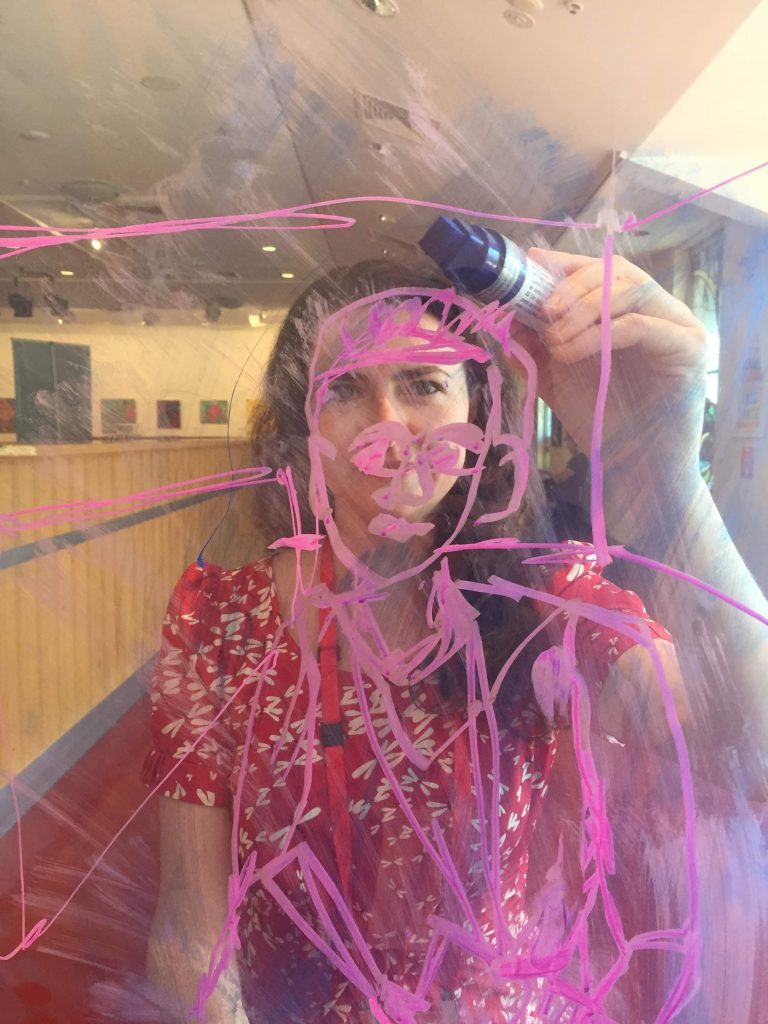 Eine junge Frau, die mit einem rosa Bleistift auf einer Glasoberfläche zeichnet