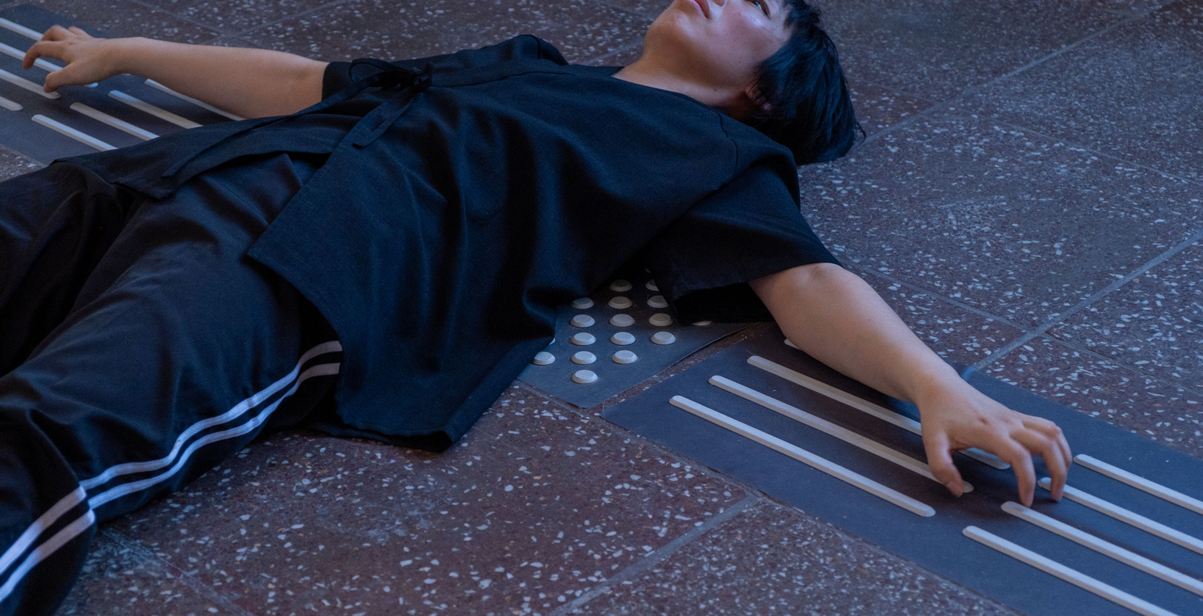 A woman lies on the floor with arms outstretched, beneath her is a black and white tactile floor system.